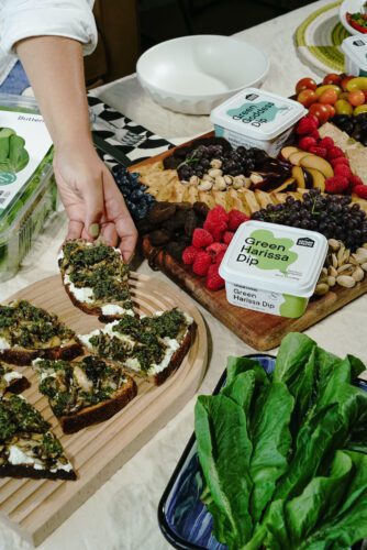 a person's hand picking up the green harissa, mushroom and ricotta crostini